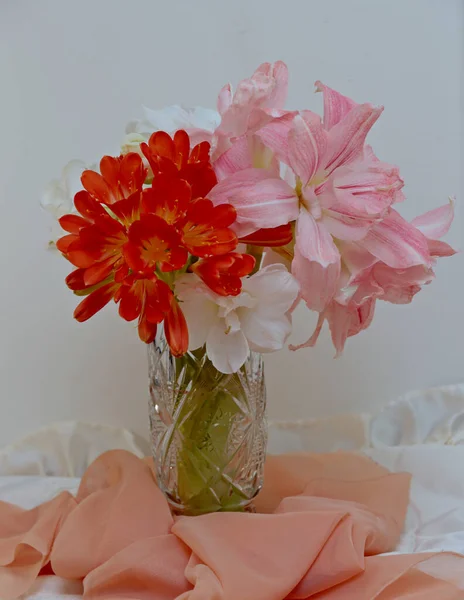 Red and pink flowers in a vase with white background and orange textile