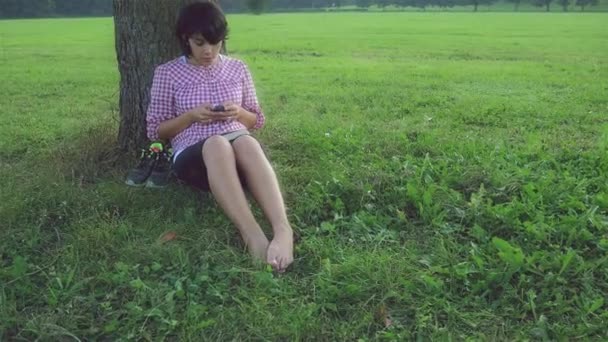 Ragazza che invia SMS sotto un albero — Video Stock