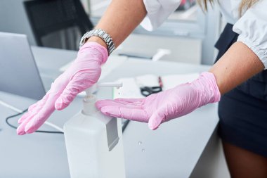 Ofiste el dezenfektanı kullanan yüz maskeli ve eldivenli bir iş kadını. Corona virüs koruması.