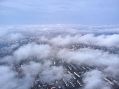 Güneşli bir günde bulutların üstünde, bir dronun manzarası. Büyük şehir evleri bulutların arasından görülebilir..