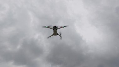 Bulutlu bir gökyüzünde uçan bir dronun yavaş çekim görüntüleri, pervaneler hızla dönüyor, dinamik bir sinematik perspektif için aşağıdan çekiliyor..