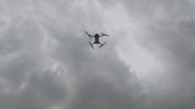 Bulutlu bir gökyüzünde uçan bir dronun yavaş çekim görüntüleri, pervaneler hızla dönüyor, dinamik bir sinematik perspektif için aşağıdan çekiliyor..