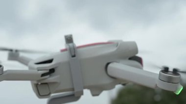 Modern insansız hava aracının uçuşa hazırlandığı yakın çekim videosu, bulutlu gökyüzüne karşı yumuşak odak içinde dönen pervaneler, gösterişli parlak tasarım ve yumuşak hareket.