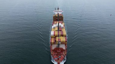 Güvertede renkli konteynırlarla sakin denizde seyreden büyük bir kargo gemisinin havadan görüntüsü. Deniz lojistiği ve küresel nakliye kavramı.