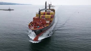 Limana yaklaşan renkli konteynırlar taşıyan büyük bir kargo gemisinin hava görüntüsü. Deniz taşımacılığı ve uluslararası nakliye kavramı.