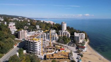 Güneşli bir günde deniz kıyısı yakınlarında kule vinçlerin inşa ettiği bir inşaat alanının havadan görüntüsü. Kentsel kalkınma kavramı.