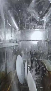 Bulaşık makinesinin içinde, bulaşıkları ve çatal bıçakları ıslatan su ile çalışan bir bulaşık makinesinin görüntüsü, makinenin içine monte edilmiş bir kameradan su altı gibi dinamik bir perspektif oluşturuyor..