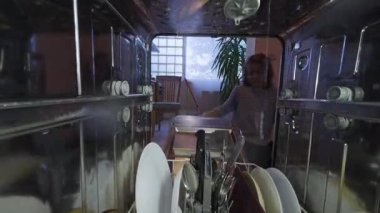 Bulaşık makinesinin içi su püskürterek bulaşıkları yıkıyordu. Sonra bir çocuk kapıyı açtı ve bir tabak almak için uzandı..