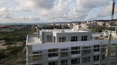 Şehir manzarası ve devam eden çalışma faaliyetleriyle çevrili, çok katlı bir binanın üzerinde çalışan bir vinç bulunan bir inşaat alanının havadan görüntüsü..