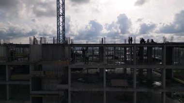 İnşaat halindeki işçilerle birlikte çok katlı beton binanın insansız hava aracı görüntüsü ve üst katlarda faaliyet gösteren bir vinç..