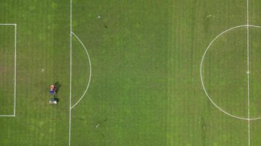 Bir futbol sahasının havadan görünüşü bir çim biçme makinesiyle çimlerin üzerinden geçiyor ve sahada açık alan işaretleri bırakıyor..