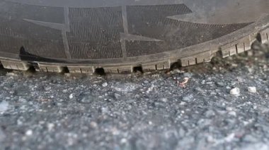 Lastik lastik izleri ve ince yol gürültüsü ile asfalt üzerinde yavaşça dönen bir araba tekerleği yakın çekim, hareket, sürtünme ve kauçuk dokusu göstermek kaldırım karşı.