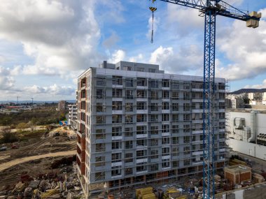 İskelelerle kaplı çok katlı bir konut inşaatı, dış duvarları bitiren işçiler, detaylı bir kentsel gelişim sahnesinde yakalandı..