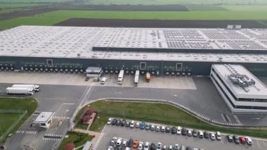 Yükleme rıhtımları ve kamyonları olan büyük bir lojistik deposunun havadan görünüşü, tarım arazileriyle çevrili dağıtım merkezi. Tedarik zinciri ve ulaşım kavramı.