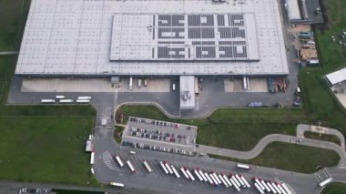 Yükleme rıhtımları, park etmiş kamyonlar ve arabaların bulunduğu bir lojistik deposunun yukarıdan aşağıya bakan görüntüsü organize ulaşım altyapısı ve tedarik zinciri operasyonlarını gösteriyor.
