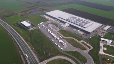 Otoyolun yakınındaki büyük bir lojistik ve dağıtım merkezinin hava görüntüsü, depoları, park edilmiş kamyonları ve tarımsal alanlarla çevrili yükleme alanlarıyla. Tedarik zinciri kavramı.