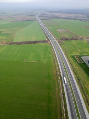 Yol boyunca giden bir kamyonla yeşil tarım tarlalarından geçen uzun bir otoyolun havadan görünüşü. Kırsal arazi, ulaşım, lojistik, altyapı ve seyahat kavramı.
