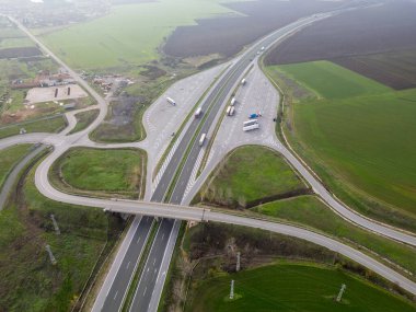 Yeşil ve tarımsal tarlalarla çevrili bir otoyol kavşağının havadan görüntüsü. Ulaşım altyapısı, lojistik, trafik akışı, kırsal arazi ve hareketlilik kavramı.