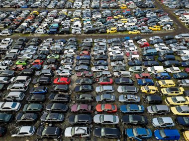 Sıraya dizilmiş eski, hasarlı ve parçalanmış araçlarla dolu terk edilmiş bir araba mezarlığının hava görüntüsü. Otomotiv atıkları, geri dönüşüm ve çevresel bozulma kavramı.