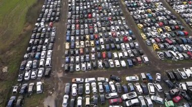 Sıraya dizilmiş eski, hasarlı ve parçalanmış araçlarla dolu terk edilmiş bir araba mezarlığının hava görüntüsü. Otomotiv atıkları, geri dönüşüm ve çevresel bozulma kavramı.