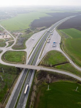 Yeşil ve tarımsal tarlalarla çevrili bir otoyol kavşağının havadan görüntüsü. Ulaşım altyapısı, lojistik, trafik akışı, kırsal arazi ve hareketlilik kavramı.