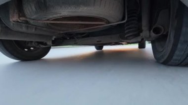 Arabanın altına monte edilmiş bir kameradan alınan POV sürücü videosu ıslak bir yolda hareket eden iniş takımlarını, tekerlekleri ve süspansiyonları gösteriyor. Dinamik otomotiv hareketi, hız, araç mekaniği ve ulaşım kavramı.