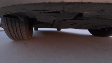 Hareket halindeki bir arabanın altına monte edilmiş, şehir asfaltında iniş takımlarını ve tekerlekleri gösteren bir kamera görüntüsü. Düşük açılı otomotiv hareketi, hız, araç mekaniği ve ulaşım kavramı.