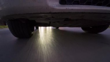 POV, arabanın altına monte edilmiş bir aksiyon kamerasından ıslak bir yolda yansımaları ve hareket bulanıklığı olan iniş ve tekerlekleri gösteren bir video. Dinamik otomotiv hareketi, hız, gece sürüşü ve ulaşım.