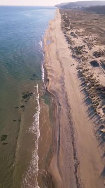 Boş kumsal ve berrak mavi gökyüzünün altında sakin deniz manzarası. Yumuşak dalgaları, kumulları ve uzak ufku olan huzurlu kıyı şeridi seyahat, doğa ve rahatlama temaları için ideal..