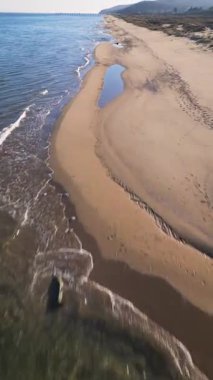 Boş kumsal ve berrak mavi gökyüzünün altında sakin deniz manzarası. Yumuşak dalgaları, kumulları ve uzak ufku olan huzurlu kıyı şeridi seyahat, doğa ve rahatlama temaları için ideal..