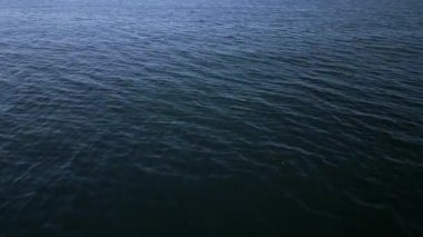 Koyu mavi denizin üzerinde, su yüzeyinde hafif dalgalanmalar olan bir uçuş. Sakin deniz dokusu ve doğal hareket, arka plan, doğa, seyahat ve atmosferik video projeleri için ideal.