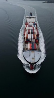 Sakin denizde yüzen konteynır gemisinin yukarıdan aşağıya doğru görüntüsü simetrik bir uyanış yaratıyor. Küresel taşımacılık, lojistik, ticaret ve deniz taşımacılığını temsil eden kargo gemisi hareket halinde.