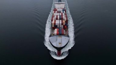 Sakin denizde yüzen konteynır gemisinin yukarıdan aşağıya doğru görüntüsü simetrik bir uyanış yaratıyor. Küresel taşımacılık, lojistik, ticaret ve deniz taşımacılığını temsil eden kargo gemisi hareket halinde.