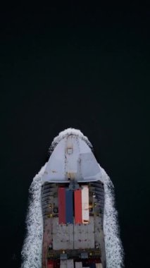 Koyu suları kesen konteyner gemisinin yukarıdan aşağıya doğru görüntüsü beyaz izi bırakıyor. Hareket halindeki kargo gemisi, küresel taşımacılık, lojistik, ticaret ve deniz taşımacılığının sembolü.