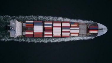 Koyu suları kesen konteyner gemisinin yukarıdan aşağıya doğru görüntüsü beyaz izi bırakıyor. Hareket halindeki kargo gemisi, küresel taşımacılık, lojistik, ticaret ve deniz taşımacılığının sembolü.