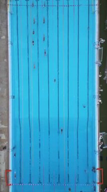 Yüzme havuzunun yukarıdan aşağı görüntüsü. Yüzücüler şeritler boyunca hareket ediyor. Mavi suyla temiz geometrik kompozisyon, spor, spor, spor, eğitim ve yaz tatili temaları için ideal.