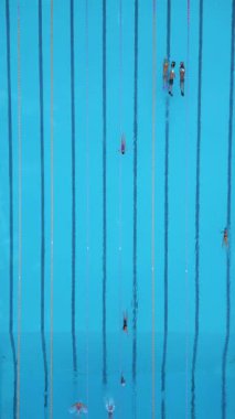 Yüzme havuzunun yukarıdan aşağı görüntüsü. Yüzücüler şeritler boyunca hareket ediyor. Mavi suyla temiz geometrik kompozisyon, spor, spor, spor, eğitim ve yaz tatili temaları için ideal.