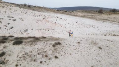 Anne ve çocuk açık arazide kumlu yolda yokuş yukarı yürüyorlar. Doğa içinde aile yolculuğu desteği, birlikteliği, keşfi ve basit açık hava macerasını sembolize eder..