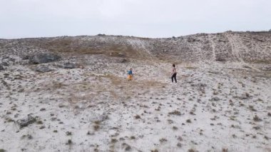 Anne ve çocuk açık kayalık arazide topla oynuyorlar. Geniş doğal çevrede neşe, hareket ve bağlantıyı ifade eden aile aktiviteleri.