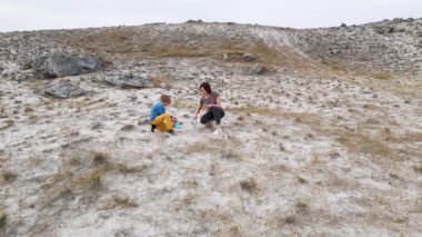 Anne ve çocuk açık kayalık arazide kumlu zemin kazıyorlar. Aile aktiviteleri merak, öğrenme ve doğada elle yapılan keşifleri gösteriyor..