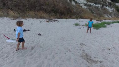 Deniz kayalıklarının yakınındaki kumsalda yakalamaç oynayan iki çocuk. Uçan top, deniz kenarında doğa ve okyanus kenarında neşeli bir çocukluk ortamı ile tasasız bir yaz oyunu..