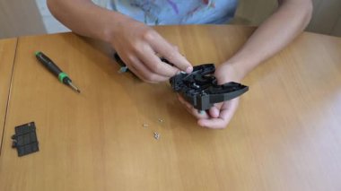 Masada küçük bir mekanik cihaz monte etmek için tornavida kullanan ellerin yakın çekimi. DIY tamir ve öğrenme süreci, el becerileri, ev ortamında odaklanma ve konsantrasyon.