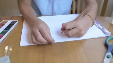 Kalem ve resimlerle dolu bir masada kağıda resim çizen bir çocuk. Yaratıcı etkinlik, öğrenme ve hayal gücü gelişimi, evde veya okulda sanat uygulaması, çocukluk eğitimi ve yaratıcılık kavramı.