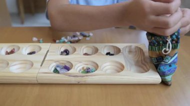 Tahta mancala seti ve taşlarla Kalah masa oyunu oynayan bir çocuk. Eğitim tablosu oyunu mantık geliştirme, sayma becerileri ve konsantrasyon, aile eğlencesi ve oyun konseptiyle öğrenme.