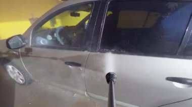 Otomobil yıkama yerinde araba kapısı ve yan aynasını yıkayan basınçlı POV videosu. Güçlü su jeti, kapalı bir yıkama hangarındaki kiri ve kiri temizliyor..
