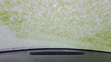 Bir işçi ön cama köpük ve su püskürtürken araba yıkama servisi aracın içinden görüldü. Cam aracılığıyla POV görünümü, kentsel self-servis araba yıkama, günlük rutin, gerçek yaşam anı.