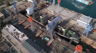 Endüstriyel bir limandaki kuru rıhtım, vinç ve kargo gemileriyle dolu bir gemi tamirhanesinin havadan görüntüsü. Büyük tersane altyapısı, deniz sanayii, lojistik ve su kenarı onarım operasyonları.