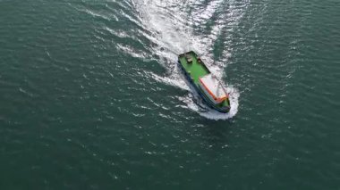 Açık denizde ilerleyen bir römorkörün havadan görünüşü koyu mavi suda beyaz bir iz bırakıyor. Denizcilik çekici gemi hareket halinde, gemi ve liman konseptleri için yukarıdan yakalandı..