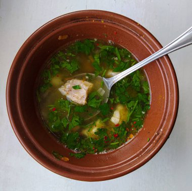 Etli, maydanozlu, masada kahverengi tabakta patates olan çorbanın fotoğrafı.