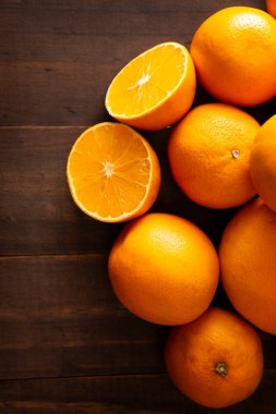 Olgun bir portakal dilimini ortadan ikiye bölüp kahverengi ahşap masa üzerinde bir sürü portakal ve fotokopi alanı ile kaplayın.